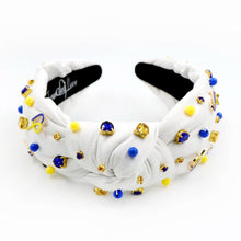 Load image into Gallery viewer, White padded headband with a twisted design, adorned with vibrant blue, yellow gemstones and down syndrome awareness charms. 