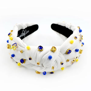 White padded headband with a twisted design, adorned with vibrant blue, yellow gemstones and down syndrome awareness charms. 
