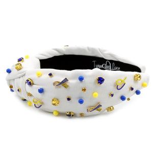 White padded headband with a twisted design, adorned with vibrant blue, yellow gemstones and down syndrome awareness charms. 