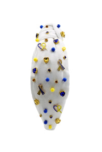 White padded headband with a twisted design, adorned with vibrant blue, yellow gemstones and down syndrome awareness charms. 
