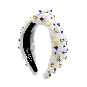 White padded headband with a twisted design, adorned with vibrant blue, yellow gemstones and down syndrome awareness charms. 
