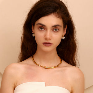 Woman wearing a gold necklace and heart gold plated earrings against a beige background