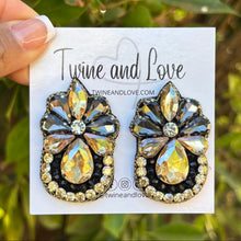 Load image into Gallery viewer, A model showcasing elegant statement earrings against an orange background.