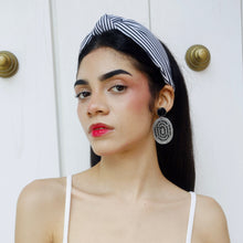 Load image into Gallery viewer, An elegant woman showcasing a striped headband and striking earrings against a neutral background.