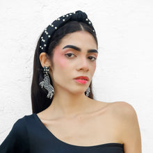 Load image into Gallery viewer, Elegant woman wearing a black pearl-embellished knotted headband and zebra-shaped beaded statement earrings against a white backdrop.