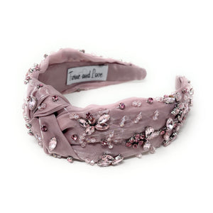 Elegant pink headband adorned with sparkling crystals and gemstones. The luxurious fabric is delicately ruched, creating a sophisticated and glamorous look.