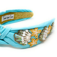 Load image into Gallery viewer, Close-up of a smiling woman accessorized with a beaded blue headband and pearl star statement earrings in a natural setting.