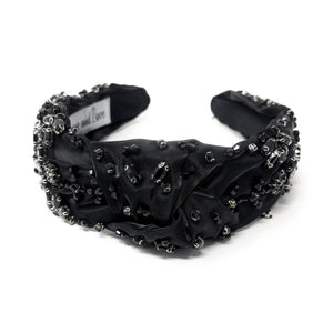 Elegant black headband adorned with sparkling crystals and gemstones. The luxurious fabric is delicately ruched, creating a sophisticated and glamorous look.