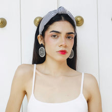 Load image into Gallery viewer, A stylish young woman wearing a white top and striped headband with bold earrings
