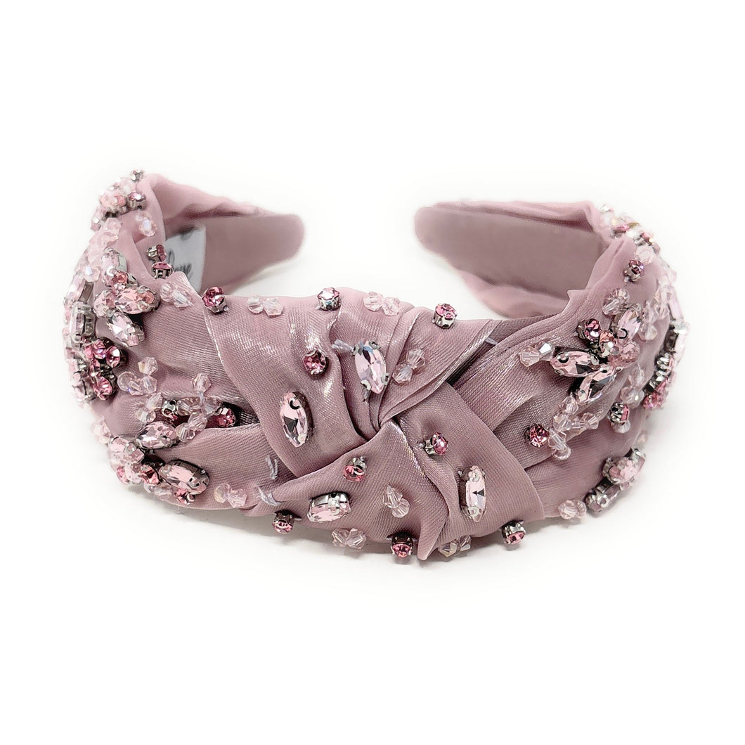 Elegant pink headband adorned with sparkling crystals and gemstones. The luxurious fabric is delicately ruched, creating a sophisticated and glamorous look.