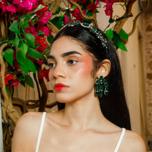 Load image into Gallery viewer, Model wearing an emerald jeweled headband and matching green statement earrings surrounded by vibrant floral decor.