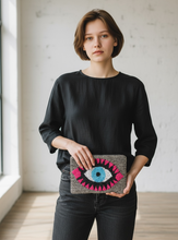 Load image into Gallery viewer, Woman holding a clutch with an eye design in a minimal indoor setting
