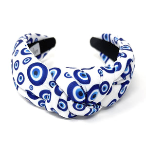 White and blue headband with a knot design featuring an evil eye pattern. The design is vibrant and playful, giving a trendy and stylish feel.