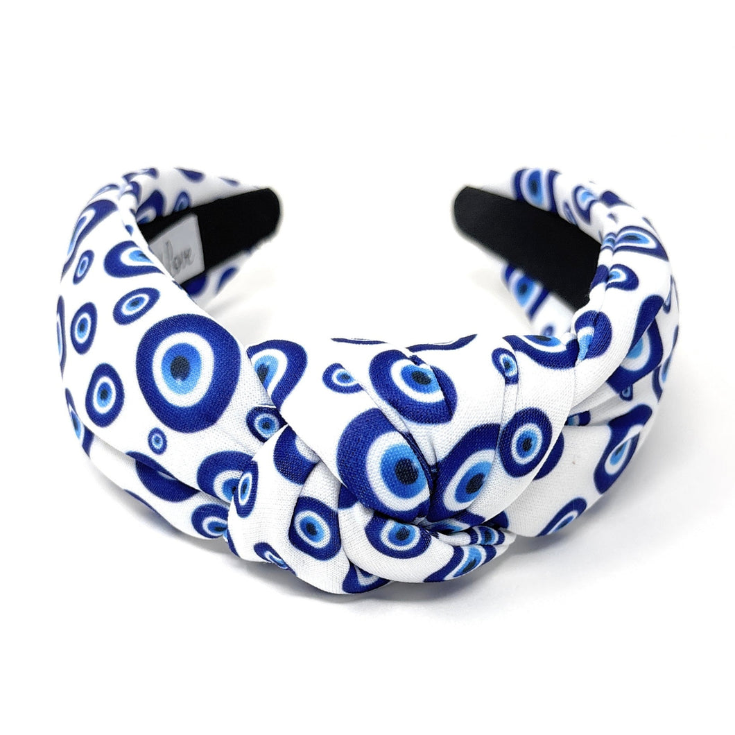 White and blue headband with a knot design featuring an evil eye pattern. The design is vibrant and playful, giving a trendy and stylish feel.