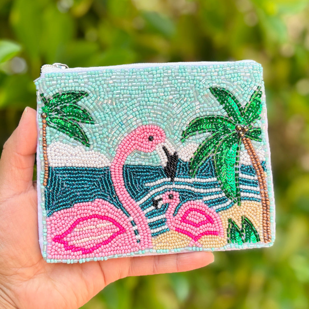 A beaded tropical pouch featuring pink flamingos, palm trees, and waves against a turquoise sky. The design is vibrant and playful, with a beachy vibe.