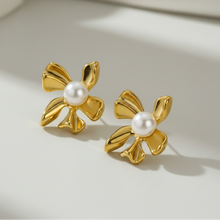 Load image into Gallery viewer, A pair of gold flower-shaped stud earrings with a white pearl at the center, resting on a clean white surface with soft shadows.