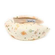 Load image into Gallery viewer, Cream-colored headband with a floral pattern in orange and green. It has a knotted design and visible label inside. Elegant and playful tone.