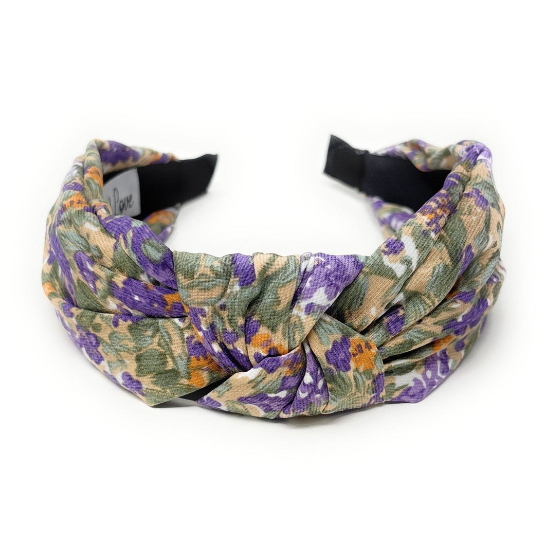 Floral headband featuring a twisted design with purple, green, and beige hues. The soft fabric and intricate pattern convey an elegant, feminine tone.