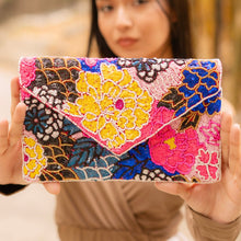 Load image into Gallery viewer, A woman showcasing a vibrant, colorful beaded clutch bag with floral designs.