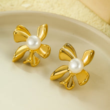 Load image into Gallery viewer, A pair of gold flower-shaped stud earrings with a central white faux pearl, displayed on a light beige ceramic dish.