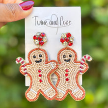 Load image into Gallery viewer, Beaded gingerbread man earrings with smiling faces and candy cane arms. Red and white beads form buttons, with red and clear rhinestone studs. Festive and playful.