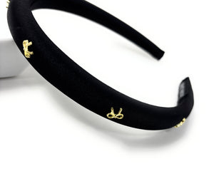 Elegant black satin headband adorned with small gold bow embellishments, displayed against a plain white background, conveying a stylish and chic tone.