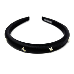 Elegant black satin headband adorned with small gold bow embellishments, displayed against a plain white background, conveying a stylish and chic tone.