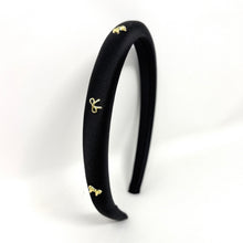 Load image into Gallery viewer, Elegant black satin headband adorned with small gold bow embellishments, displayed against a plain white background, conveying a stylish and chic tone.