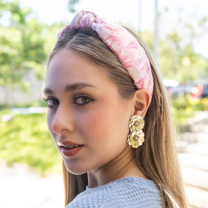 Woman wearing a pink headband and gold color floral earrings outdoors