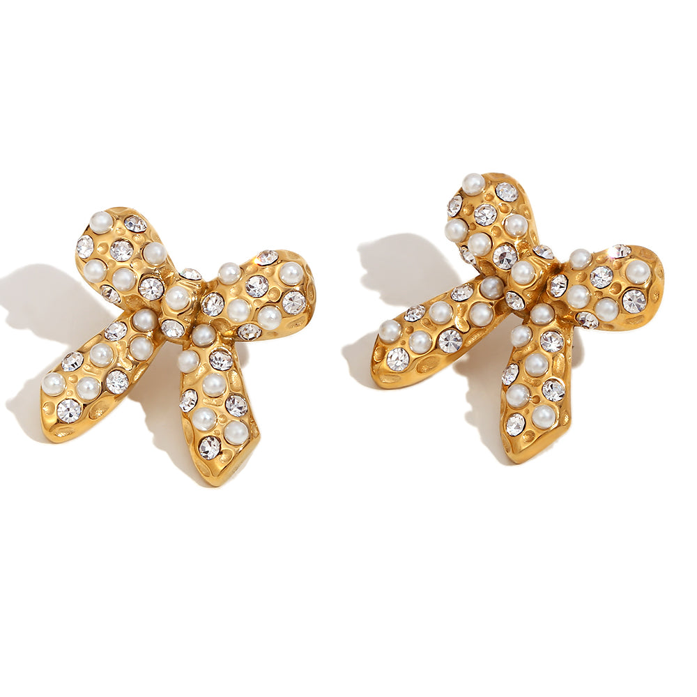 Gold bow-shaped earrings adorned with pearls and rhinestones on a white background, casting soft shadows, conveying elegance and luxury.