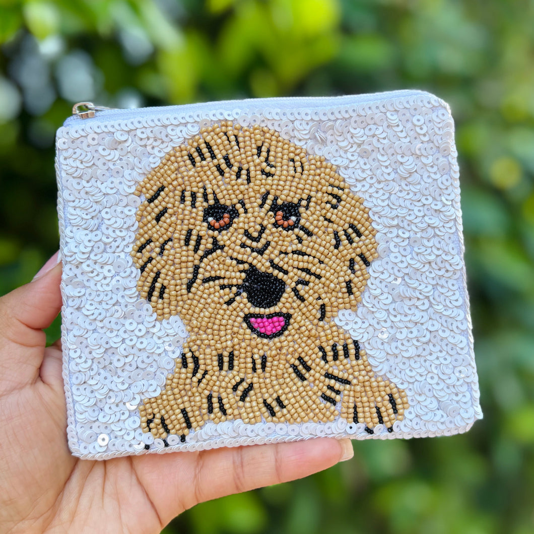 A small white sequin clutch features a beaded dog face with black details and a pink tongue. The design adds a playful, textured element.