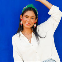 Load image into Gallery viewer, Woman in white shirt and blue jeans wearing a green holiday headband posing against a blue background