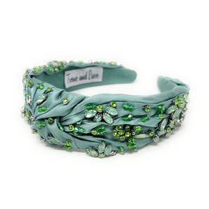Elegant green headband adorned with sparkling crystals and gemstones. The luxurious fabric is delicately ruched, creating a sophisticated and glamorous look.