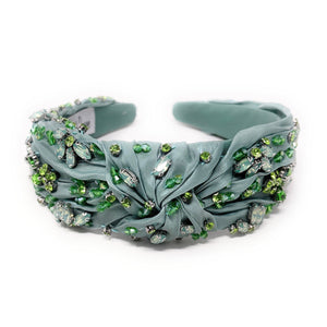 Elegant green headband adorned with sparkling crystals and gemstones. The luxurious fabric is delicately ruched, creating a sophisticated and glamorous look.