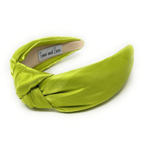 A vibrant green satin headband with a twisted knot design, labeled "True and Love" inside. The fabric's sheen adds a touch of elegance.