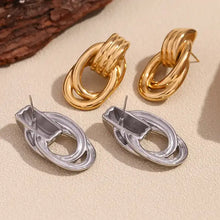 Load image into Gallery viewer, Gold and silver tone earrings with oval loops and ridged details, resembling linked chains. They convey a modern and elegant style, set against a plain white background.