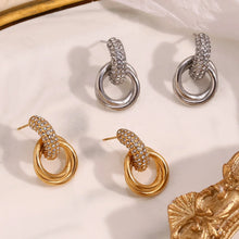 Load image into Gallery viewer, Pair of 18k gold plated and silver hoop earrings on a beige surface with decorative elements.