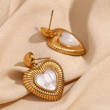 Load image into Gallery viewer, Gold heart-shaped earrings with a ribbed texture and a central mother-of-pearl heart. They hang from small gold spheres, evoking elegance and romance.