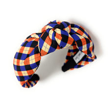 Load image into Gallery viewer, Colorful headband with a plaid pattern in red, blue, and beige hues against a white background. The fabric is knotted in the center, creating a playful and trendy accessory.