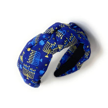 Load image into Gallery viewer, A fabric headband with a knotted twist design, featuring a blue background with a gold and light blue menorah and star pattern, shown on a white background.