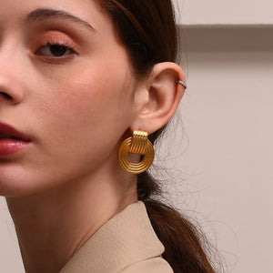 Close-up of a woman wearing gold drop earrings with a neutral background