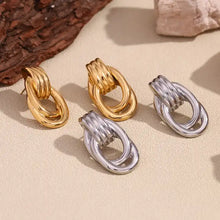 Load image into Gallery viewer, Gold-tone earrings with oval loops and ridged details, resembling linked chains. They convey a modern and elegant style, set against a plain white background.