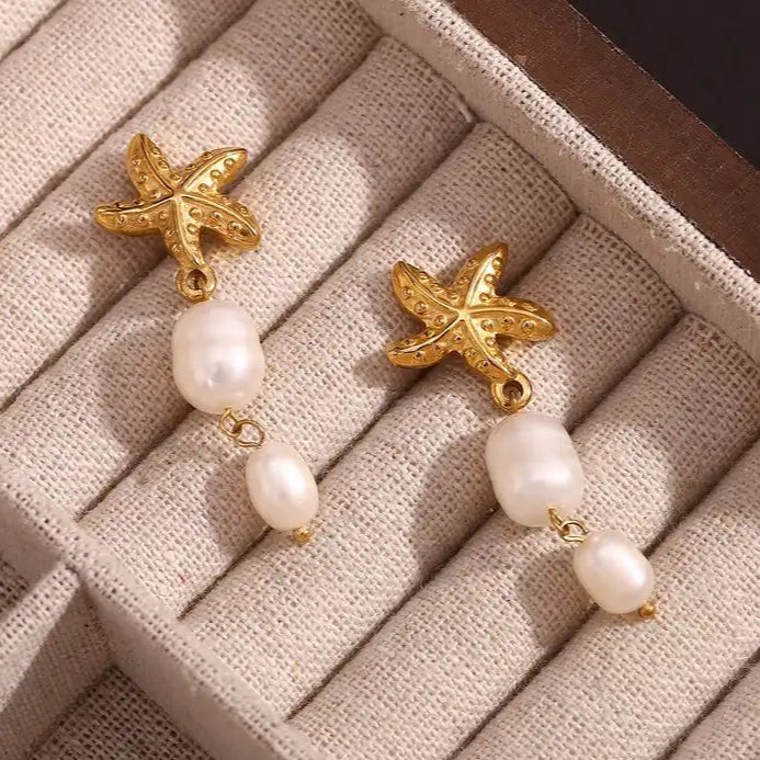 Gold starfish earrings with pearl drops on a textured surface