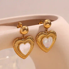 Load image into Gallery viewer, Gold heart-shaped earrings with a ribbed texture and a central mother-of-pearl heart. They hang from small gold spheres, evoking elegance and romance.