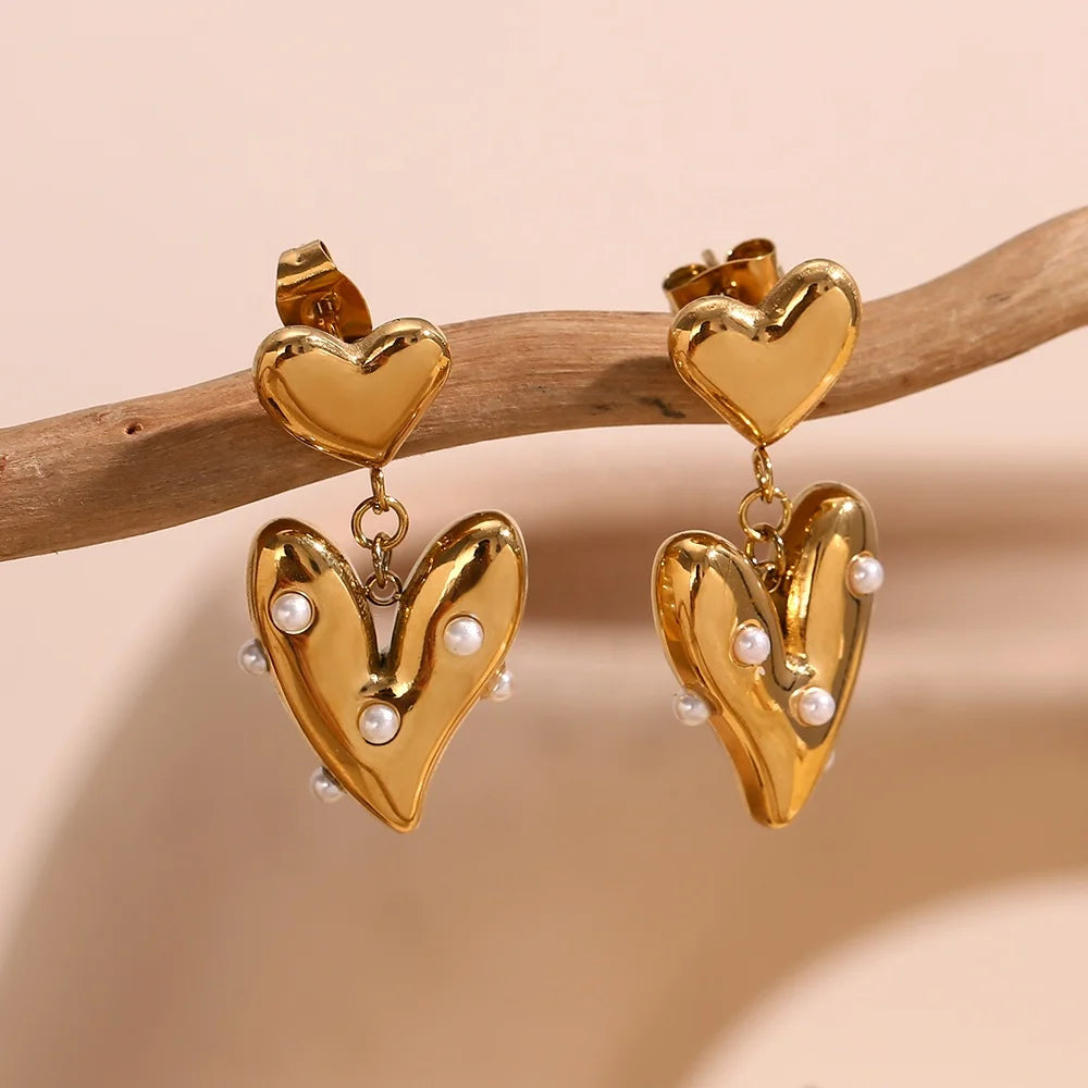 18k Gold plated heart-shaped earrings with pearl accents on a beige background