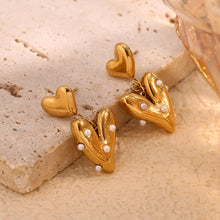 Load image into Gallery viewer, Gold heart-shaped earrings with pearl accents on a beige stone surface