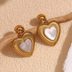 Gold heart-shaped earrings with a ribbed texture and a central mother-of-pearl heart. They hang from small gold spheres, evoking elegance and romance.