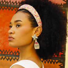 Load image into Gallery viewer, Woman wearing a colorful headband and &quot;Here to Party&quot; earrings against an orange and black patterned background