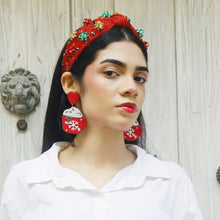 Load image into Gallery viewer, Woman wearing a white shirt and red headpiece with holiday bow decorations against a wooden door background.