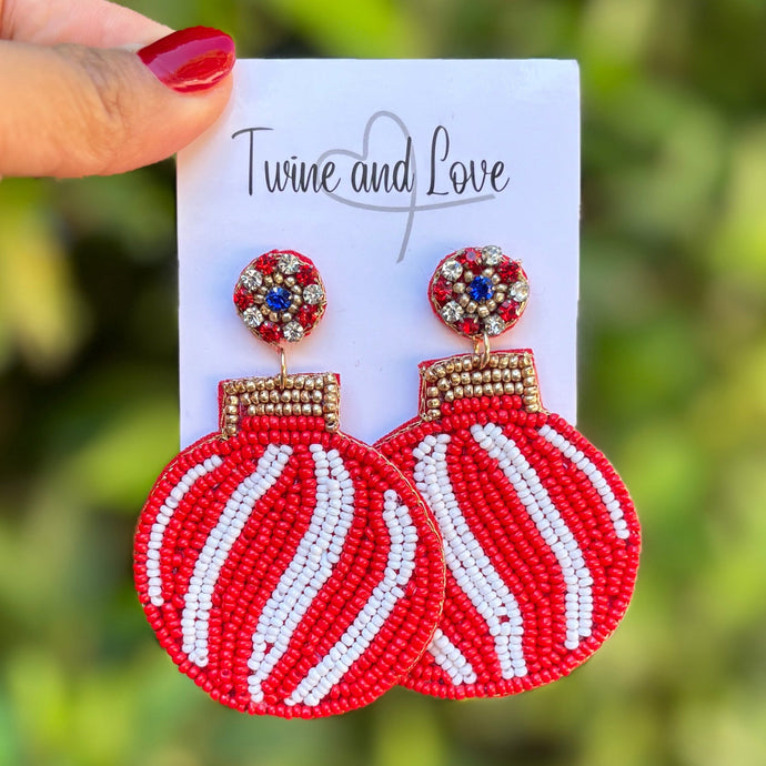 Two festive beaded earrings featuring red baubles with white swirl patterns and gold tops. The tops have small colored beads, enhancing their vibrant look.